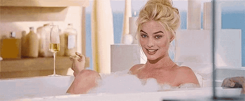 a woman is taking a bath with a glass of champagne .