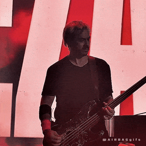 a man is playing a bass guitar in front of a red and white sign
