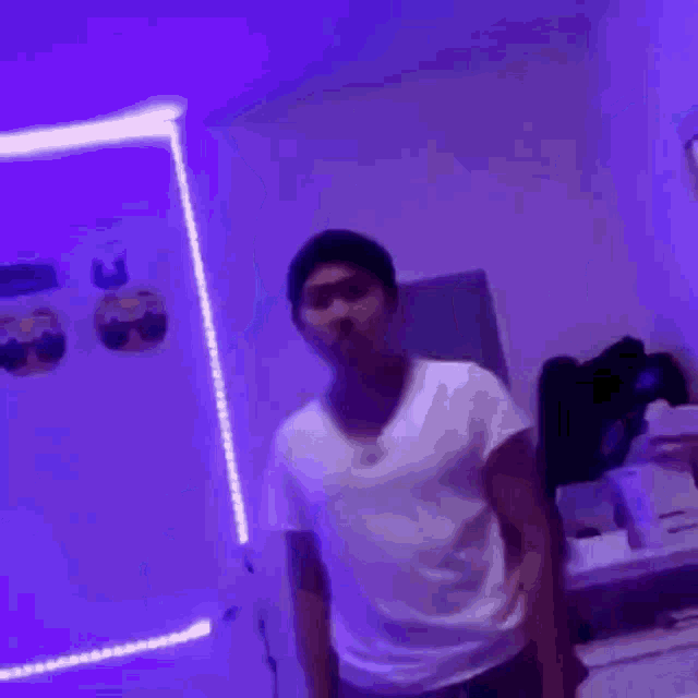 a young man in a white shirt is dancing in a room with purple lights .