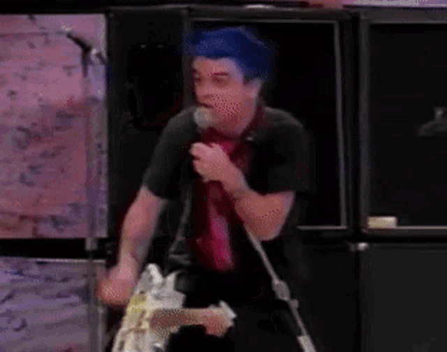 a man with blue hair is singing into a microphone on stage