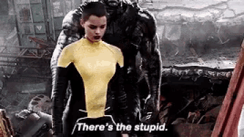 a woman in a yellow suit is standing next to a man in a black suit and says `` there 's the stupid '' .