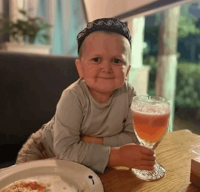 a little boy is sitting at a table with a glass of beer