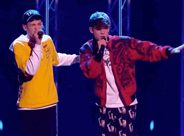 two men singing into microphones with one wearing a yellow shirt that says " off white " on it