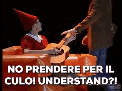 a man in a red hat is holding a guitar while a woman in a red dress sits in an orange chair .