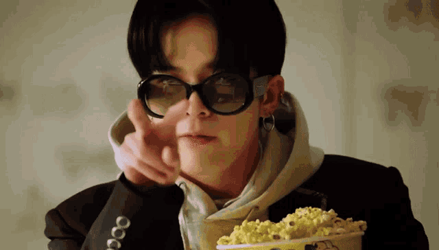 a young man wearing sunglasses and a hoodie is holding a bucket of popcorn