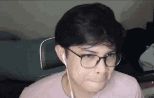 a man wearing glasses and ear buds is making a face .