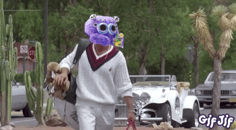 a man with a purple monster on his head walks down a street with a stop sign in the background