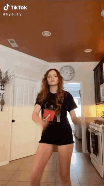 a woman is dancing in a kitchen with a clock on the ceiling
