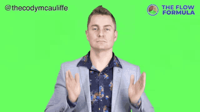 a man in a suit and a floral shirt is making a gesture with his hands on a green screen .