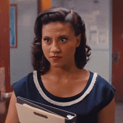 a woman in a blue dress is holding a binder and looking at the camera