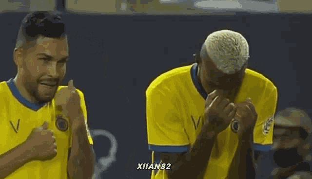 two soccer players covering their faces with their hands while wearing yellow jerseys with the number 82 on the bottom