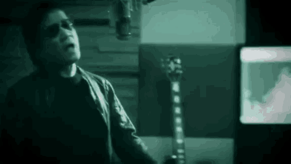 a man wearing sunglasses is singing into a microphone in a dark room .
