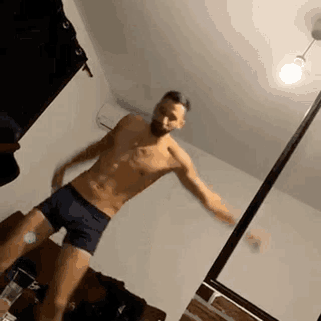 a shirtless man in blue boxer shorts is dancing in a room