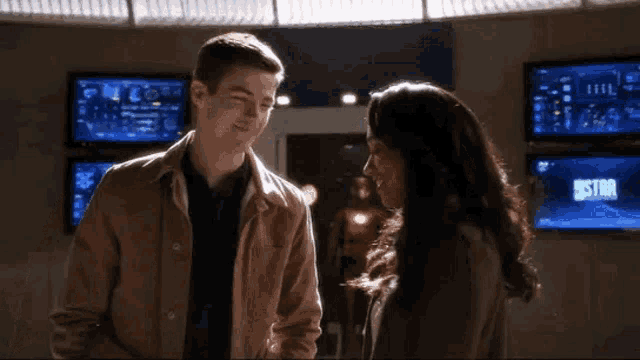 a man and a woman are standing next to each other in a room with monitors .