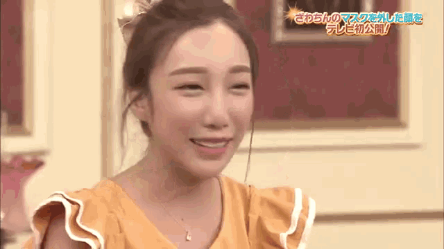 a woman in a yellow dress with ruffled sleeves is smiling in front of a wall with chinese writing