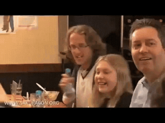 a group of people are sitting at a table in a restaurant with the website www.sakuragon.org in the corner .