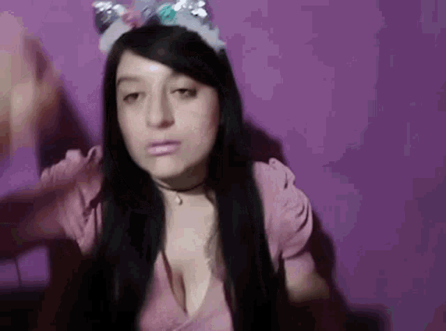 a woman with long black hair is wearing a unicorn headband and a pink shirt .