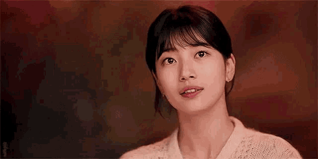 a close up of a woman 's face with a red background . she is wearing a white sweater and earrings .