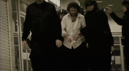 a man in a white shirt is being led by a group of police officers