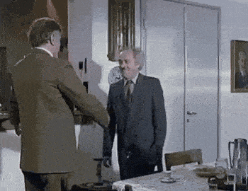 two men in suits are shaking hands in a living room in front of a table .