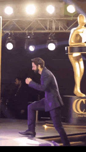 a man in a suit stands on a stage in front of a statue with the letter c on the bottom
