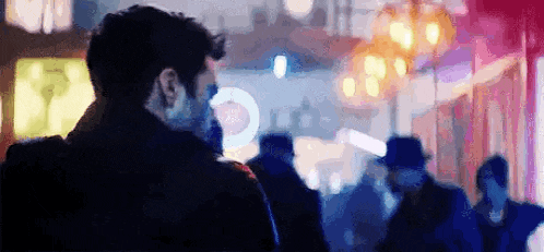 a man in a mask is standing in a crowd of people in a city at night .