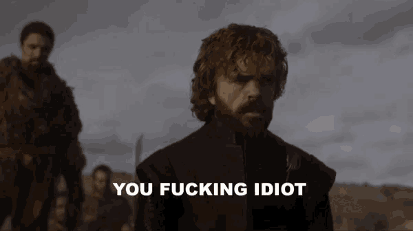 a man with a beard is standing in front of a sign that says " you fucking idiot "