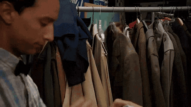 a man in a bow tie is looking at a closet full of clothes