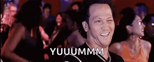 a man is making a funny face in front of a crowd and the word yuuummm is on the screen .
