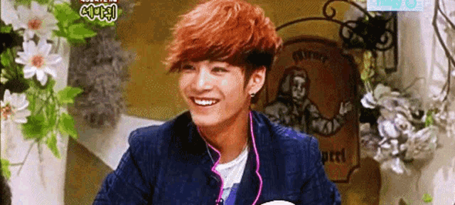 a young man with red hair is smiling in front of flowers and a sign that says ' bakery '