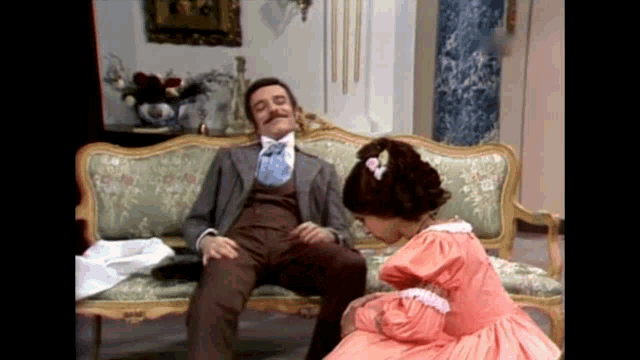 a man in a suit sits on a couch with a woman in a pink dress