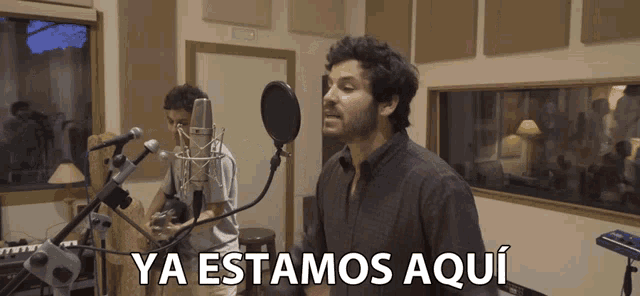 a man singing into a microphone with the words ya estamos aqui written below him