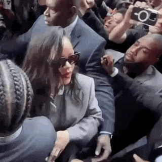 a woman in sunglasses is being escorted by a man in a suit in a crowd of people .