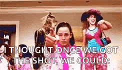 a group of women are standing next to each other in a room . one of the women is wearing a pink shirt .