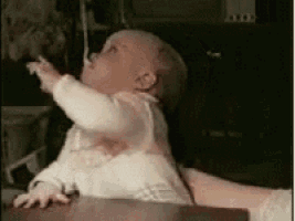 a baby is sitting on a table and reaching up towards the sky .