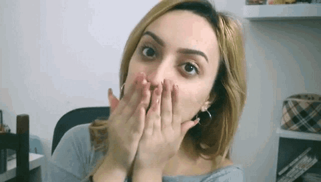 a woman is covering her mouth with her hands and looking surprised .
