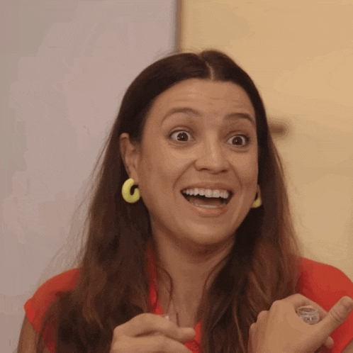 a woman wearing a red shirt and yellow earrings is smiling
