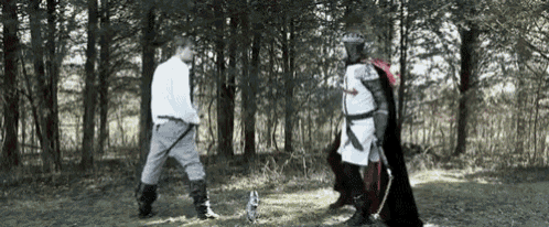 a man in a white shirt is standing next to a man in a red cape in the woods