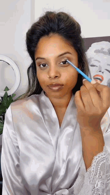 a woman in a white robe is applying eye shadow with a blue brush