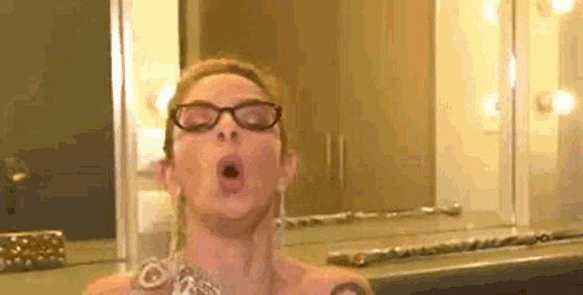 a woman wearing glasses is taking a selfie in front of a mirror in a room .