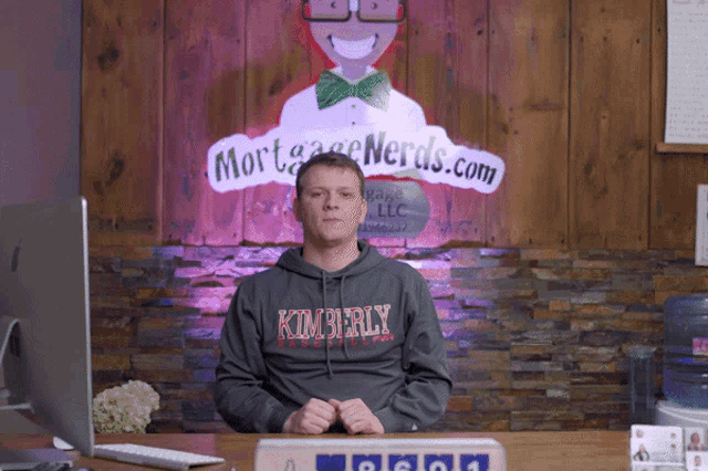 a man wearing a kimberly sweatshirt stands in front of a sign that says mortgage nerds.com