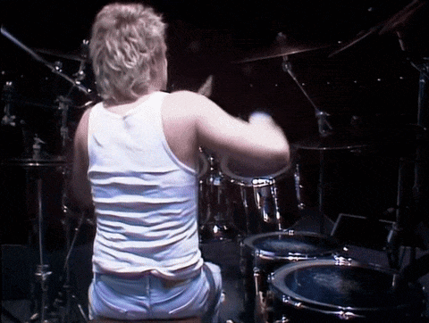 a man in a tank top is playing drums in a dark room
