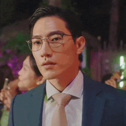 a man in a suit and tie with glasses looks at the camera