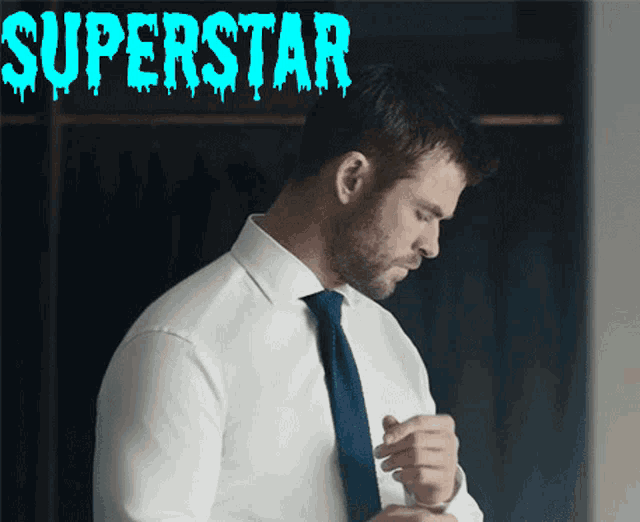 a man in a white shirt and blue tie is standing in front of a sign that says " superstar "