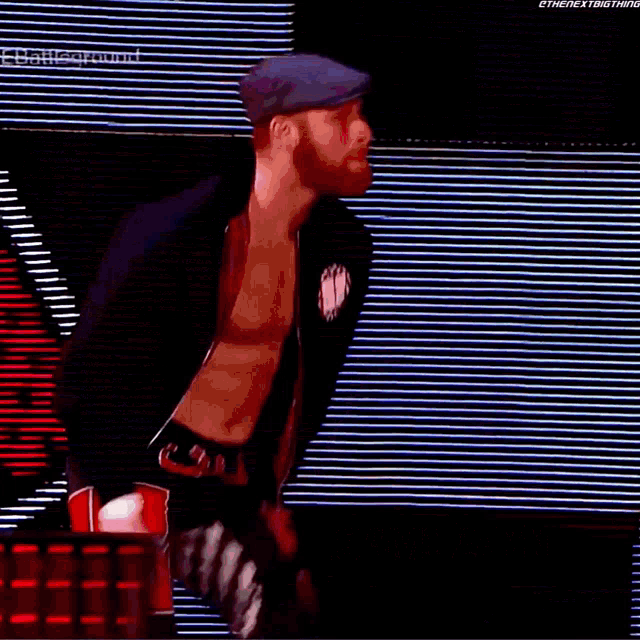 a man wearing a hat and a black jacket is walking in front of a striped wall .