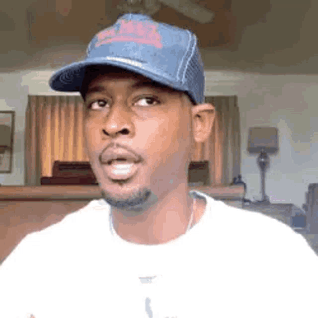 a man wearing a blue hat and a white t-shirt is making a funny face .