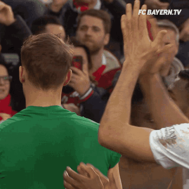 a man in a green shirt stands in front of a crowd with fc bayern.tv on the bottom
