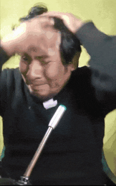 a man in a black shirt is sitting in front of a microphone and scratching his head