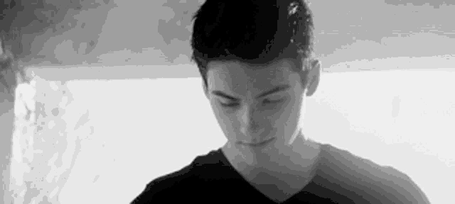 a black and white photo of a young man in a black shirt looking down .