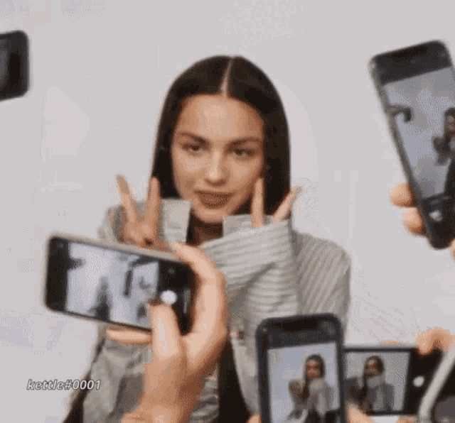 a woman is being photographed by a group of people holding their phones .